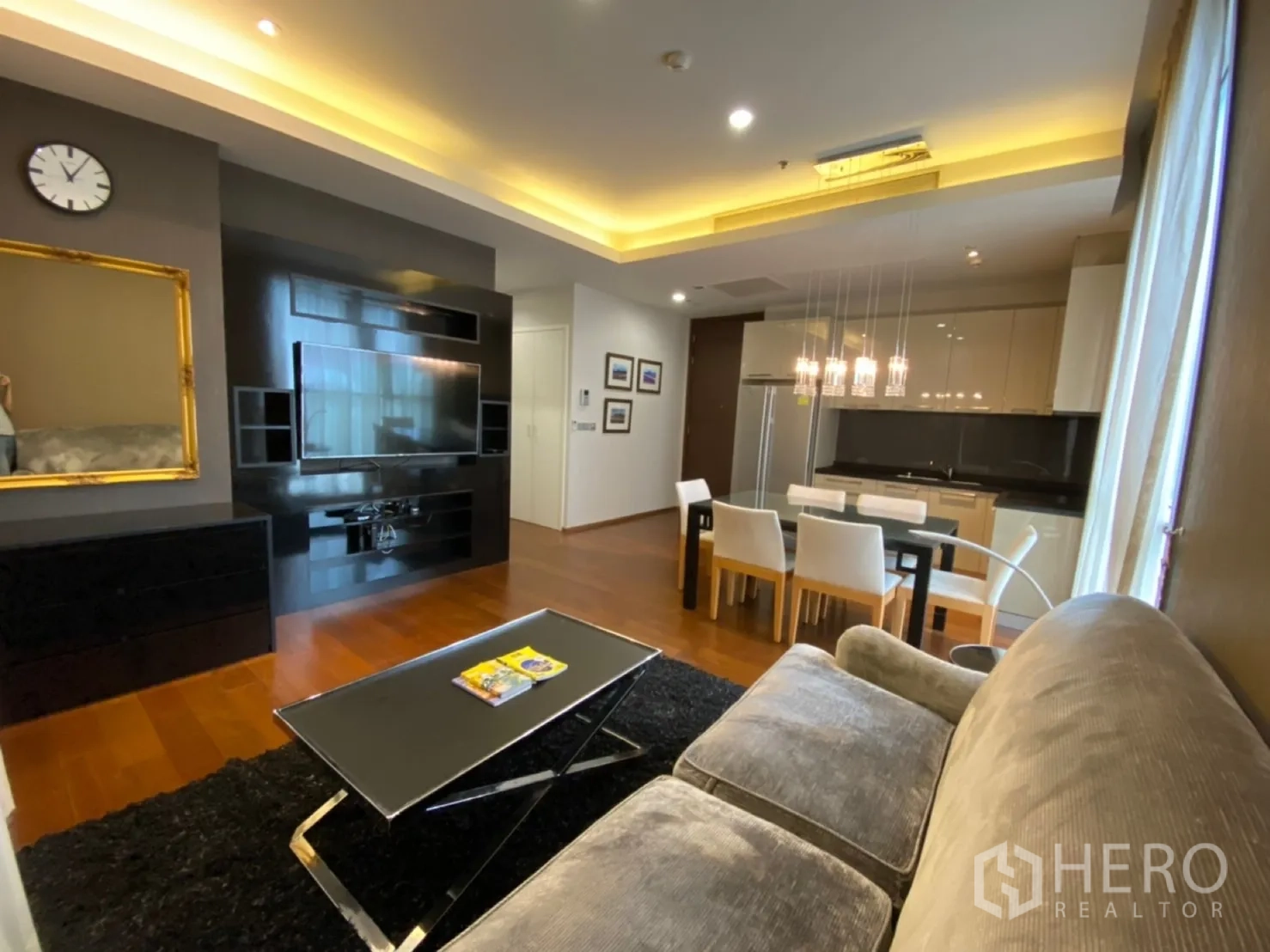 公寓 出租在Watthana, Bangkok - 从沙发望向亮面电视墙与现代厨房及餐桌。