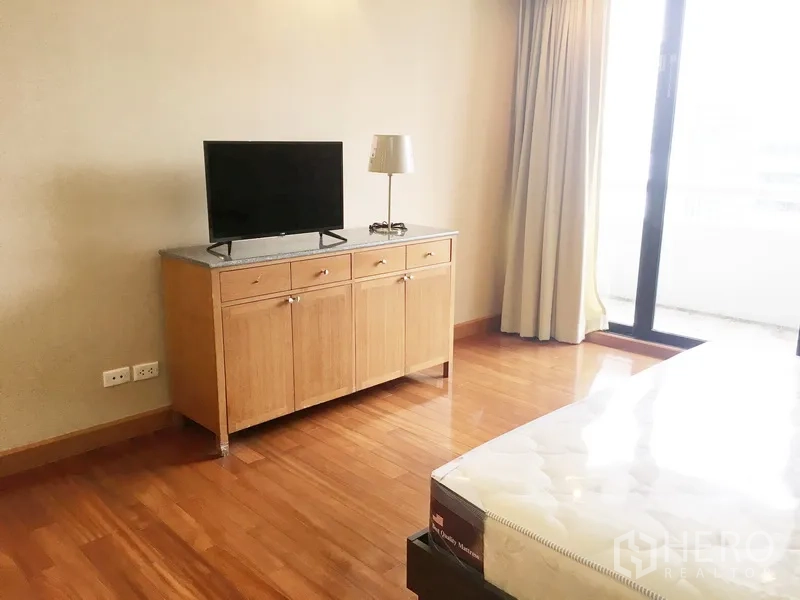 公寓 出租在Pathum Wan, Bangkok - 卧室设有电视柜，推拉玻璃门连通阳台，木地板。