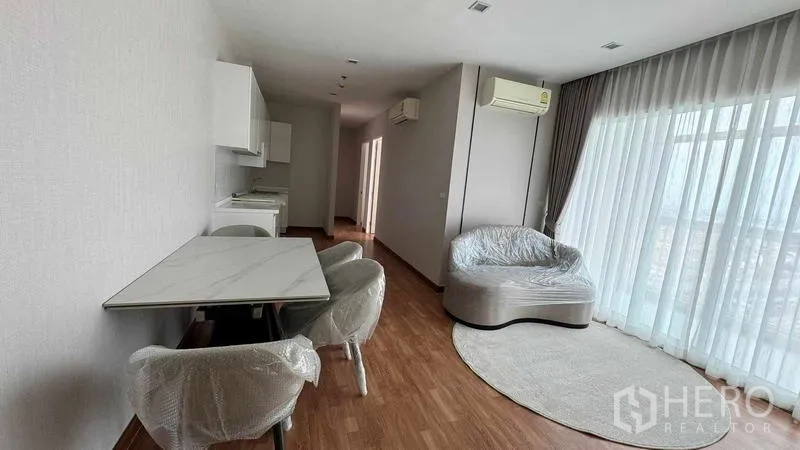 公寓 出租在Bang Na, Bangkok - 开放式起居区，圆形沙发与地毯、餐桌和大窗引入城市采光。