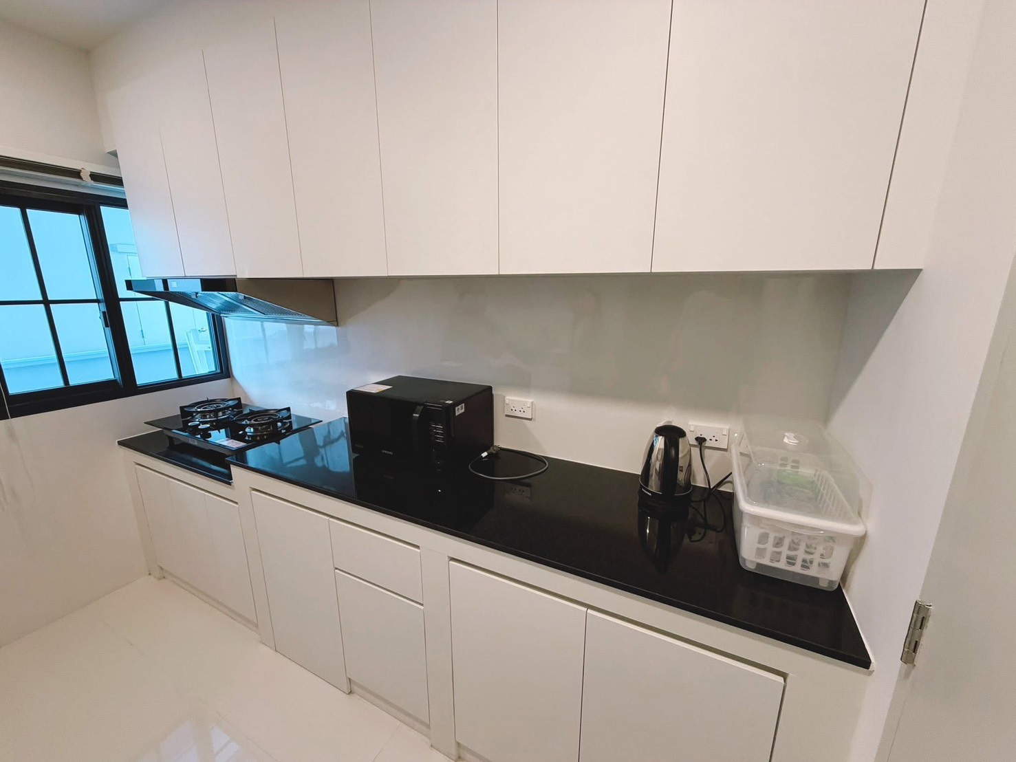 Detached House for rent in Bang Phli, Samut Prakan - Modern white kitchen with black granite countertop, gas hob, hood and a window.
