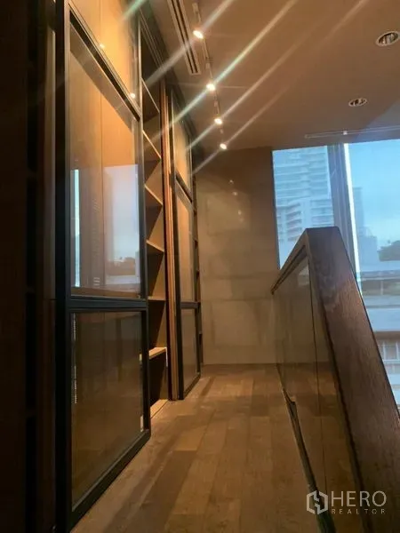 公寓 出租在Watthana, Bangkok - 夹层走廊，木地板、玻璃栏杆与内置书架，临城市窗景。