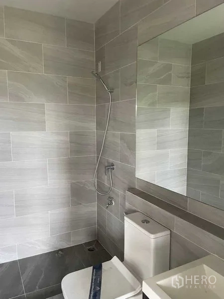 Townhouse for sale in Bueng Kum, Bangkok - Modern bathroom with gray wall tiles, shower, toilet and a large mirror.
