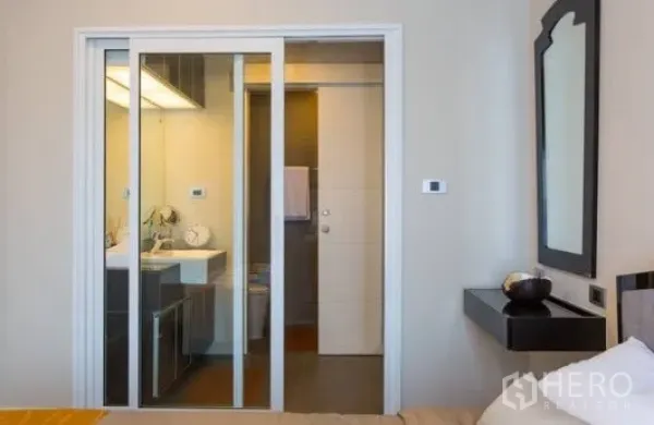 Condominium for rent in Khlong Toei, Bangkok - Bedroom view to bathroom through sliding glass doors with modern vanity.