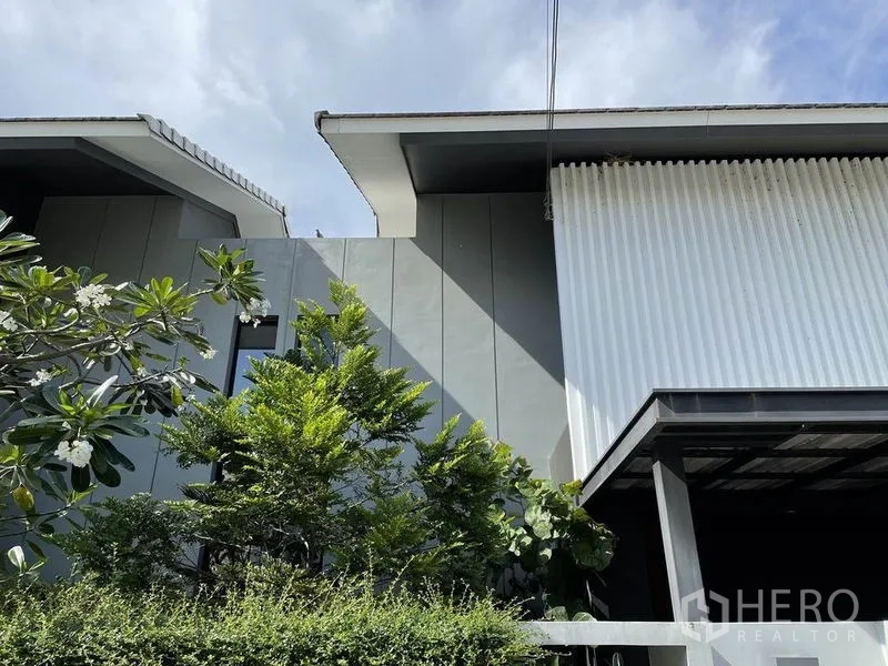 Detached House for sale in Sai Mai, Bangkok - Exterior view of rooflines framed by lush greenery and a trimmed hedge.