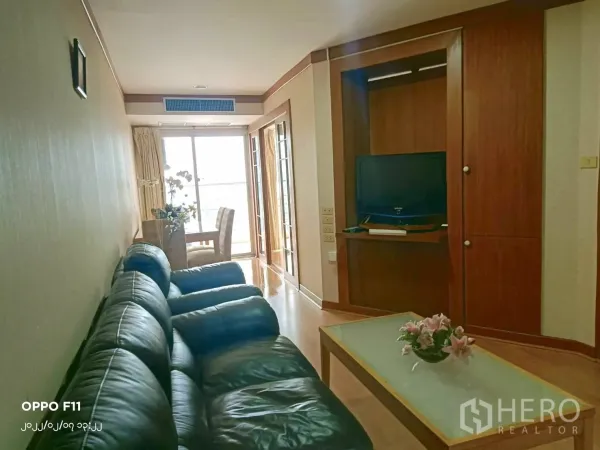 Condominium for rent in Khlong Toei, Bangkok - Long living space with black leather sofa, TV unit and a dining spot by a bright window.