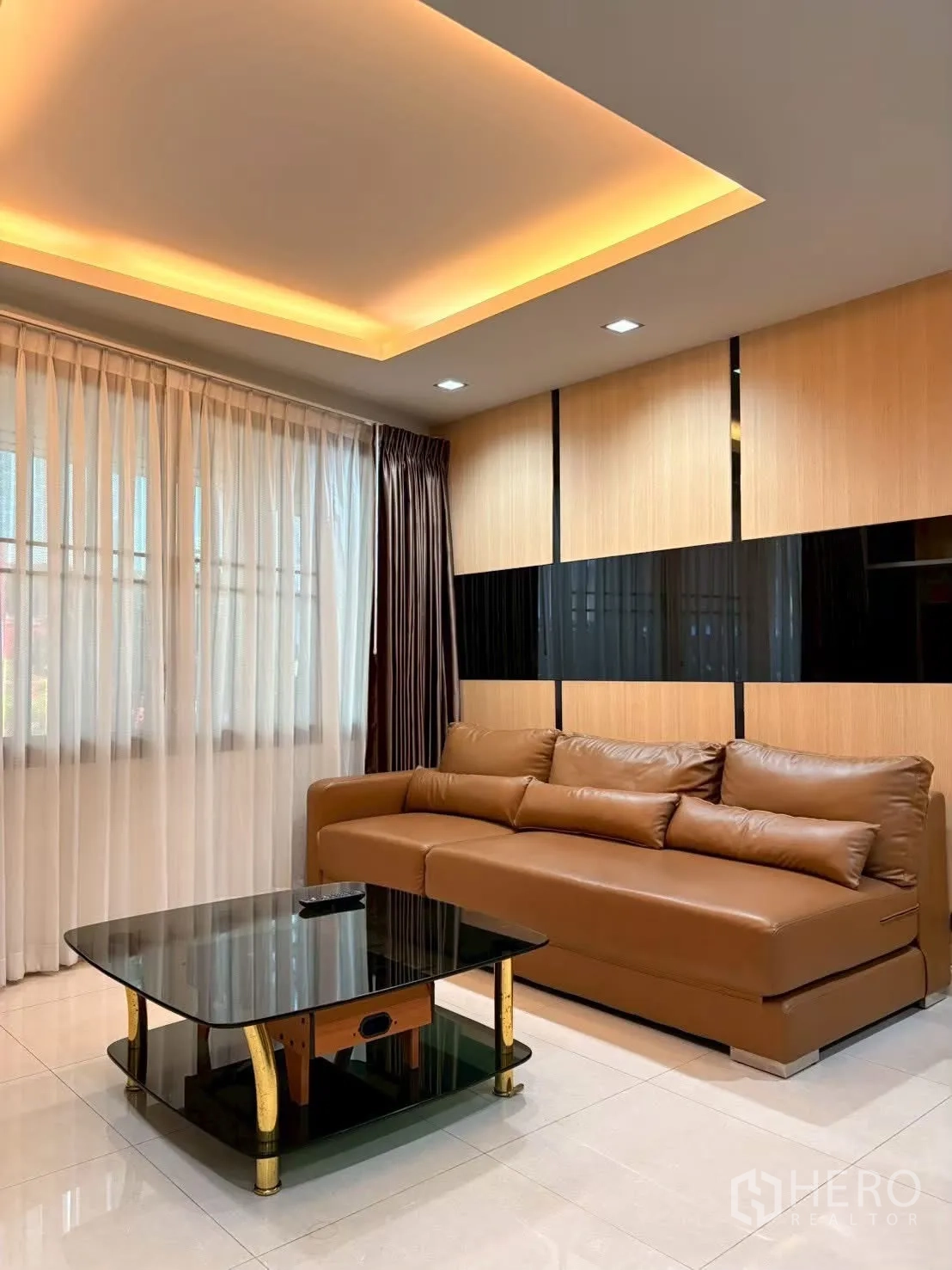 ทาวน์เฮาส์ for rent in Pathum Wan, Bangkok - ห้องนั่งเล่นโซฟาหนังสีน้ำตาล โต๊ะกระจก และไฟซ่อนฝ้าโทนอุ่น.