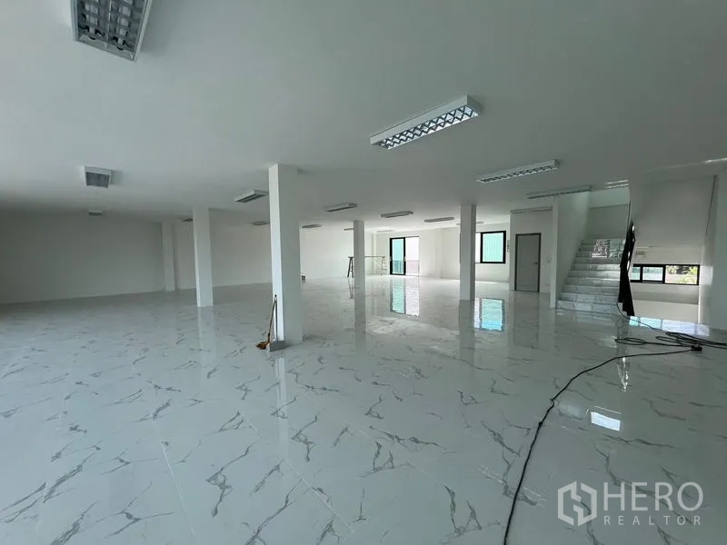Warehouse for rent in Bang Sao Thong, Samut Prakan - Expansive office floor with columns, multiple windows and access to a balcony and stairs.