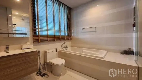 Condominium for rent in Khlong Toei, Bangkok - Bathroom with large window blinds, soaking tub, toilet and vanity.