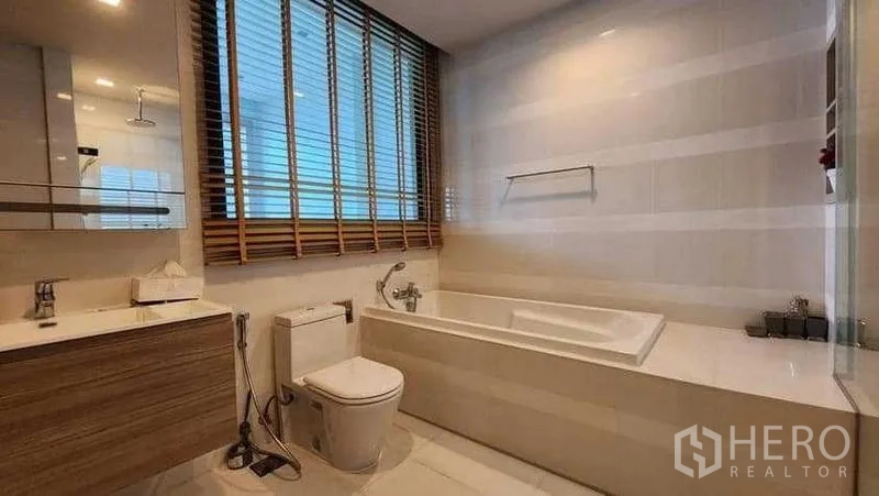 Condominium for rent in Khlong Toei, Bangkok - Bathroom with large window blinds, soaking tub, toilet and vanity.