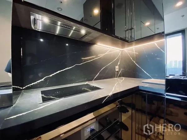 Condominium for rent in Khlong Toei, Bangkok - Sleek kitchenette with black marble backsplash, induction hob, under-cabinet lighting, and built-in oven.