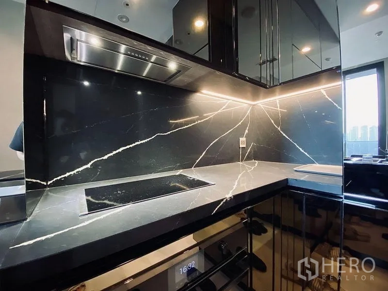 Condominium for rent in Khlong Toei, Bangkok - Sleek kitchenette with black marble backsplash, induction hob, under-cabinet lighting, and built-in oven.