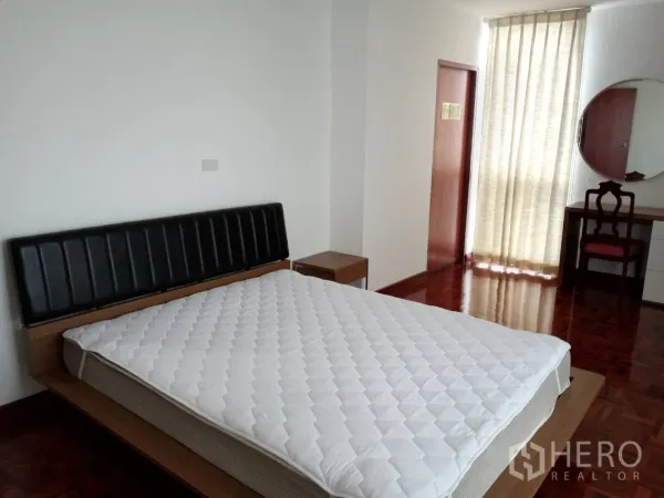 房间 出租在Watthana, Bangkok - 宽敞卧室，配大床、床头柜、梳妆台与透光窗帘。