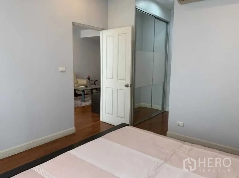 Condominium for rent in Khlong Toei, Bangkok - Bedroom view showing sliding wardrobe with mirror and doorway to living room.