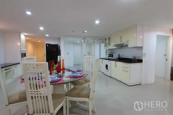 公寓 出租在Watthana, Bangkok - 开放式餐厨区，白色橱柜、四人玻璃餐桌、室内洗衣机与玻璃推拉隔断。