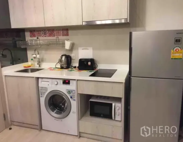 公寓 出租在Khlong Toei, Bangkok - 现代一体化厨房，白色橱柜、水槽、电炉，配洗衣机、微波炉与银色冰箱。