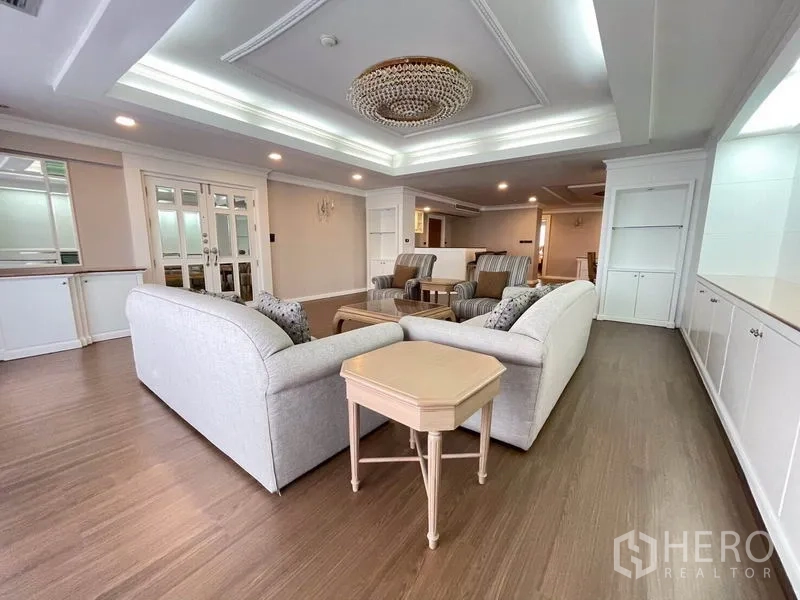 公寓 出租在Watthana, Bangkok - 宽敞客厅，格栅吊顶与水晶吊灯，木地板与成套沙发。