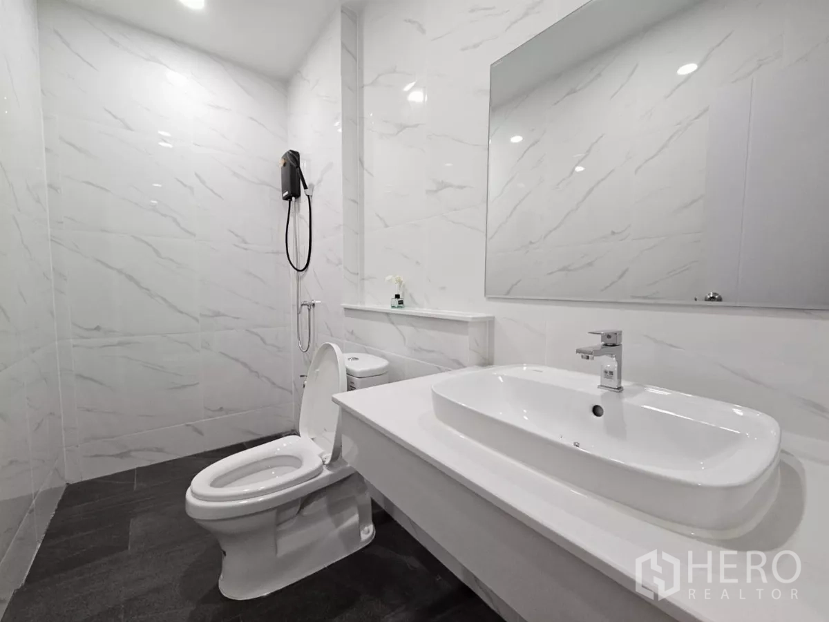 Townhouse for sale in Lat Phrao, Bangkok - Second bathroom with white marble-effect tiles, large mirror and shower.