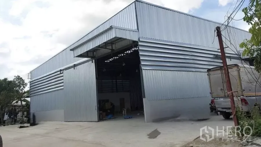 货栈 出租在Khlong Sam Wa, Bangkok - 金属外墙仓库外观，宽大推拉门与宽敞混凝土场地，便于卡车进出。
