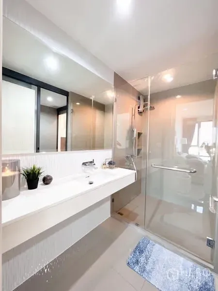 Condominium for rent or sale in Khlong Toei, Bangkok - Modern bathroom with long white vanity and glass-enclosed shower.