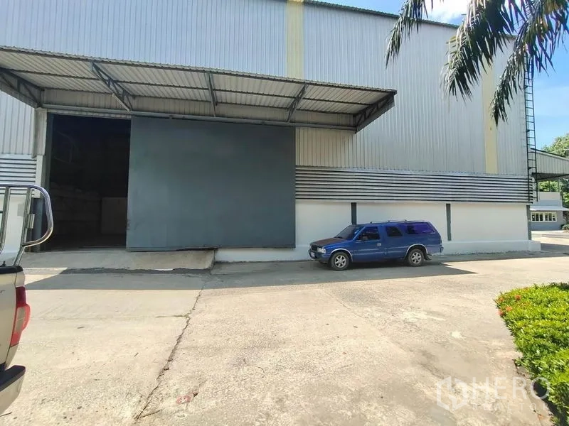 Warehouse for rent in Mueang Samut Sakhon, Samut Sakhon - Warehouse exterior with covered loading bay, oversized sliding steel door, and wide driveway.