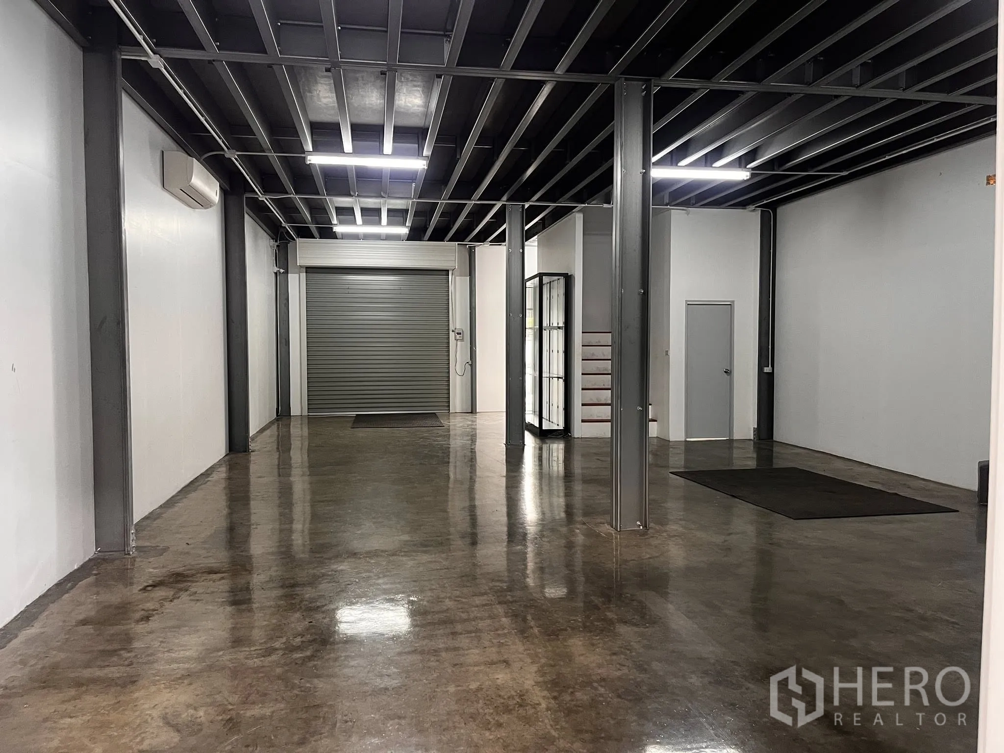 Warehouse for rent in Lat Phrao, Bangkok - Open warehouse floor with steel columns, polished concrete, bright lighting, and a roller shutter.