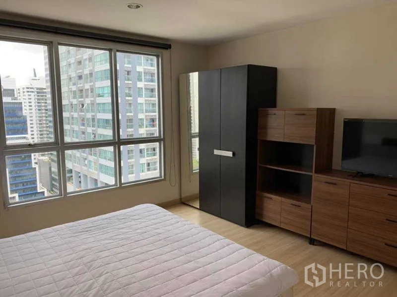 Condominium for rent in Bang Rak, Bangkok - Bedroom with city view windows, wardrobe, shelving and TV cabinet.