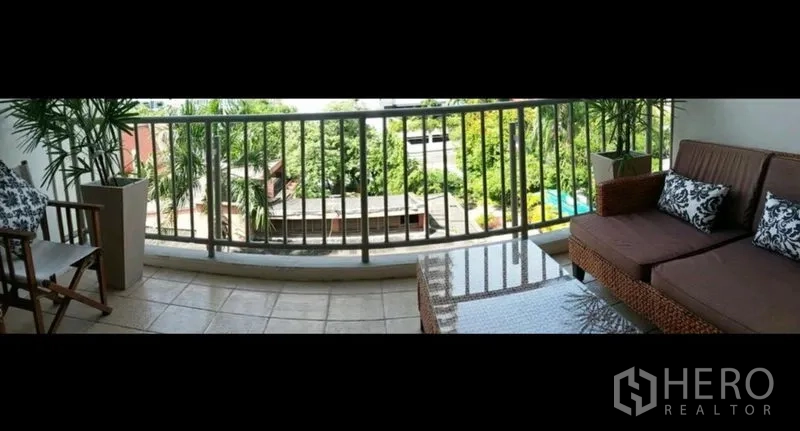 Condominium for rent in Khlong Toei, Bangkok - Spacious balcony with rattan sofa and coffee table overlooking greenery and the residence pool.