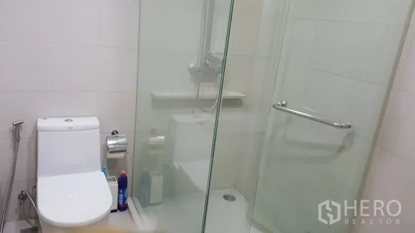 Condominium for rent in Khlong Toei, Bangkok - Modern bathroom with glass-enclosed shower and white tiled walls.
