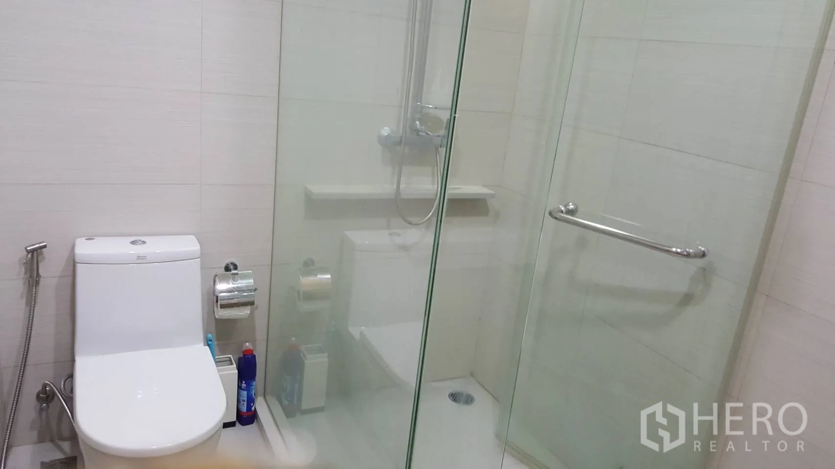 Condominium for rent in Khlong Toei, Bangkok - Modern bathroom with glass-enclosed shower and white tiled walls.