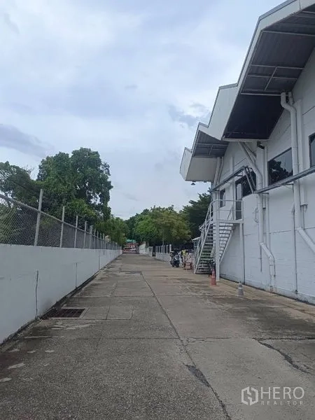 Warehouse for rent in Lam Luk Ka, Pathum Thani - Long service lane beside the warehouse with perimeter fence, trees and access for trucks.