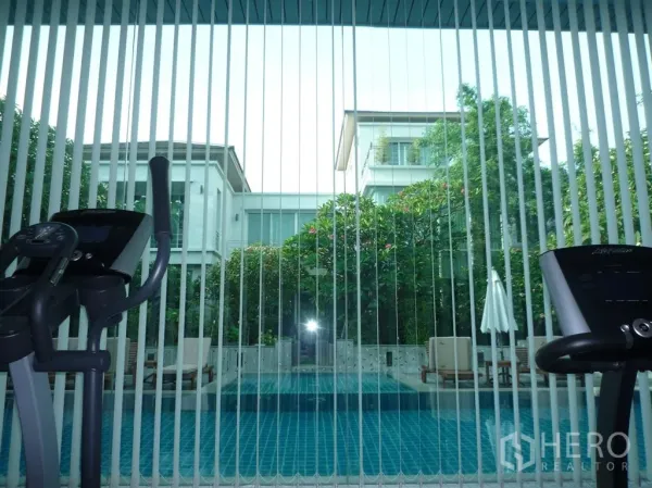 Detached House for rent in Khan Na Yao, Bangkok - Fitness room with cardio machines looking through vertical blinds to a pool.