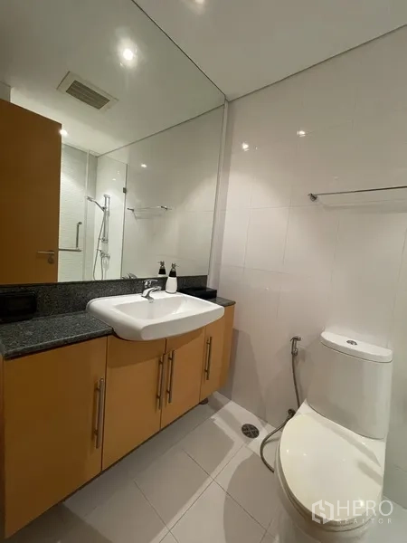 Condominium for rent or sale in Watthana, Bangkok - Second bathroom with white tiles, vanity with granite counter, toilet, and shower area.