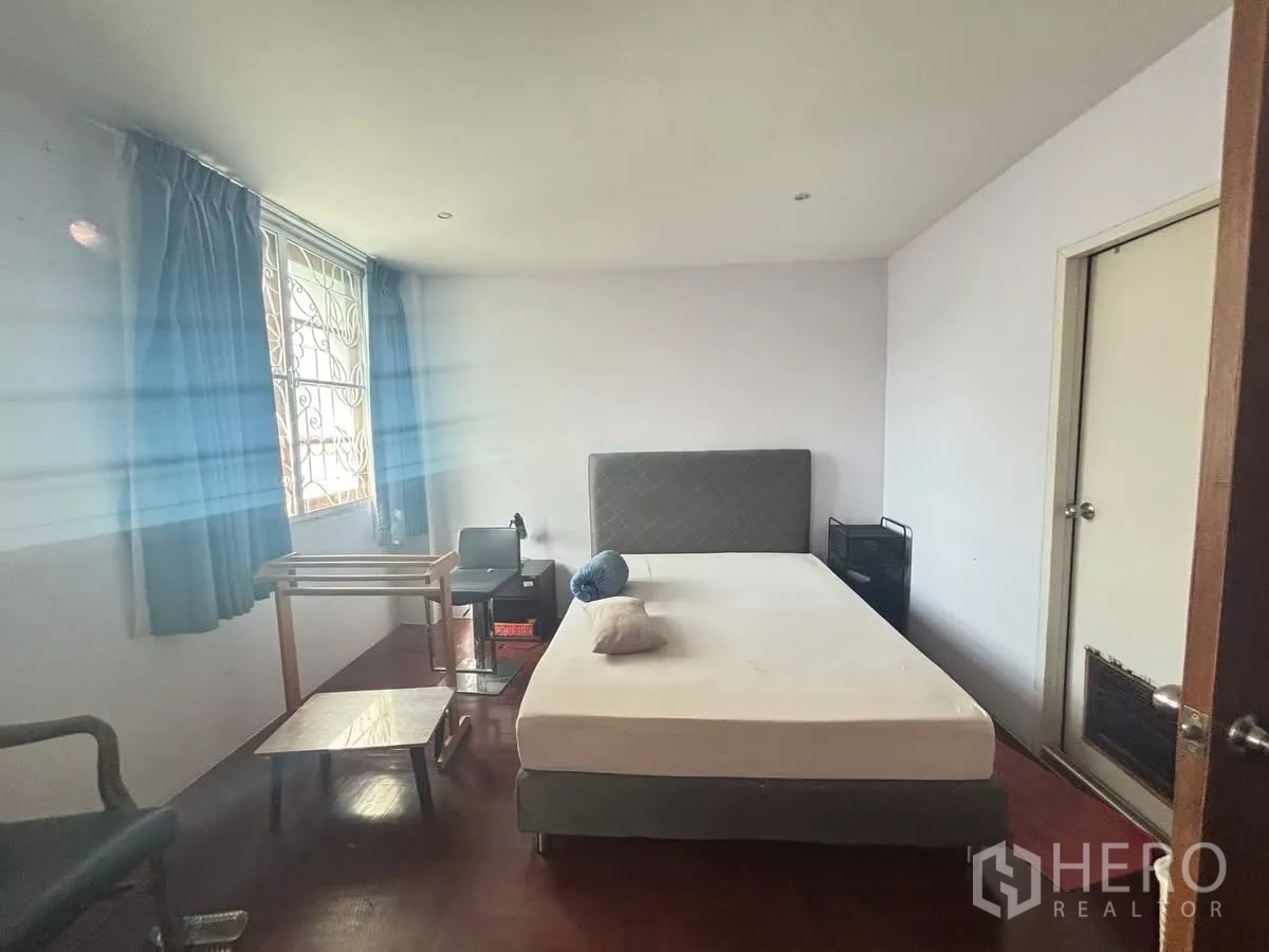 Shophouse for rent in Watthana, Bangkok - Simple bedroom with window, blue curtains and a double bed on wooden flooring.