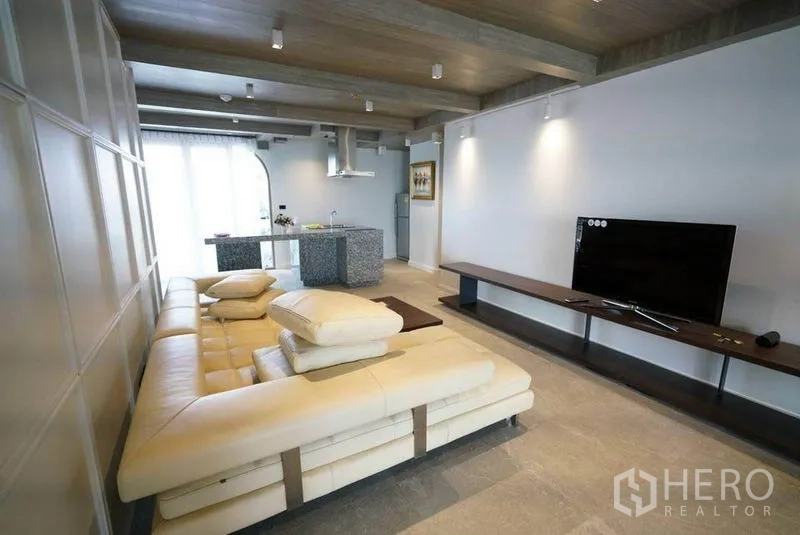 Condominium for rent or sale in Bang Na, Bangkok - Open‑plan lounge with sectional sofa, TV console and a granite kitchen island beyond.