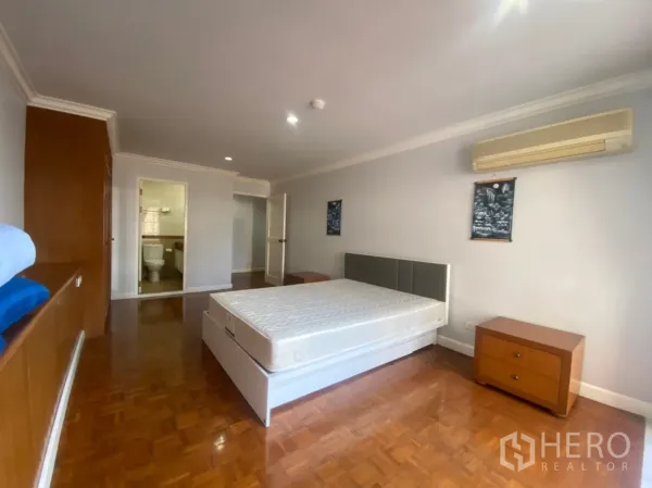 Condominium for rent or sale in Watthana, Bangkok - Bedroom with en-suite entrance, air conditioner, bedside tables and polished parquet flooring.
