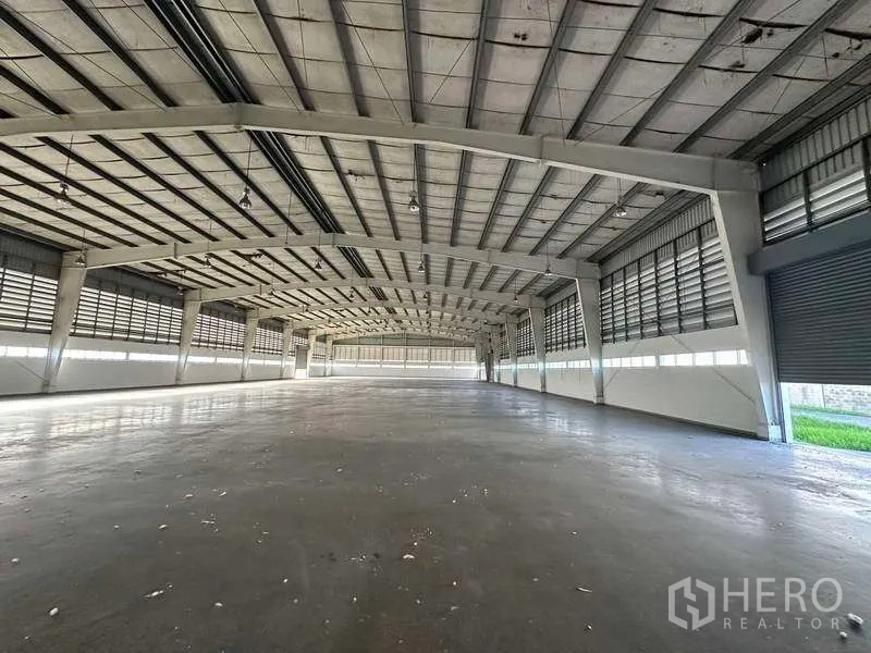 Factory for rent in Khlong Luang, Pathum Thani - Vast warehouse floor with high steel truss roof, louvered side panels and smooth concrete surface.