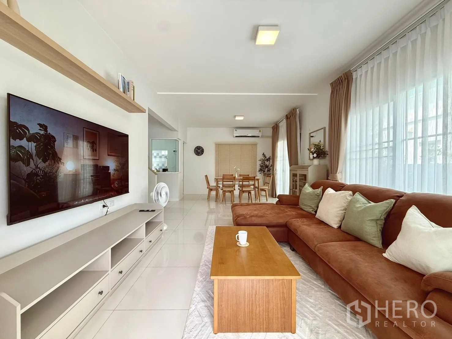 Detached House for rent in Bang Phli, Samut Prakan - Bright open-plan living room with large windows, L-shaped brown sofa, TV wall, and dining area.