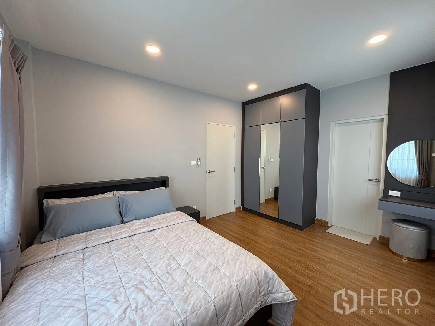 บ้าน for rent in Bang Phli, Samut Prakan - ห้องนอนพร้อมผ้าปูที่นอนสีเทา ตู้เสื้อผ้าบานกระจกและมุมโต๊ะเครื่องแป้ง บนพื้นลามิเนตลายไม้.