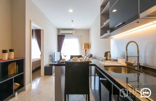 Condominium for rent in Khlong Toei, Bangkok - Galley kitchen leading to bright living area with window and TV.