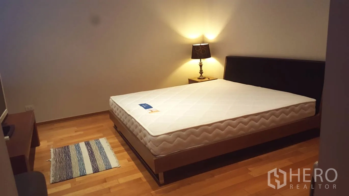 Condominium for rent or sale in Khlong Toei, Bangkok - Cozy bedroom with a queen bed, bedside lamp and hardwood flooring.