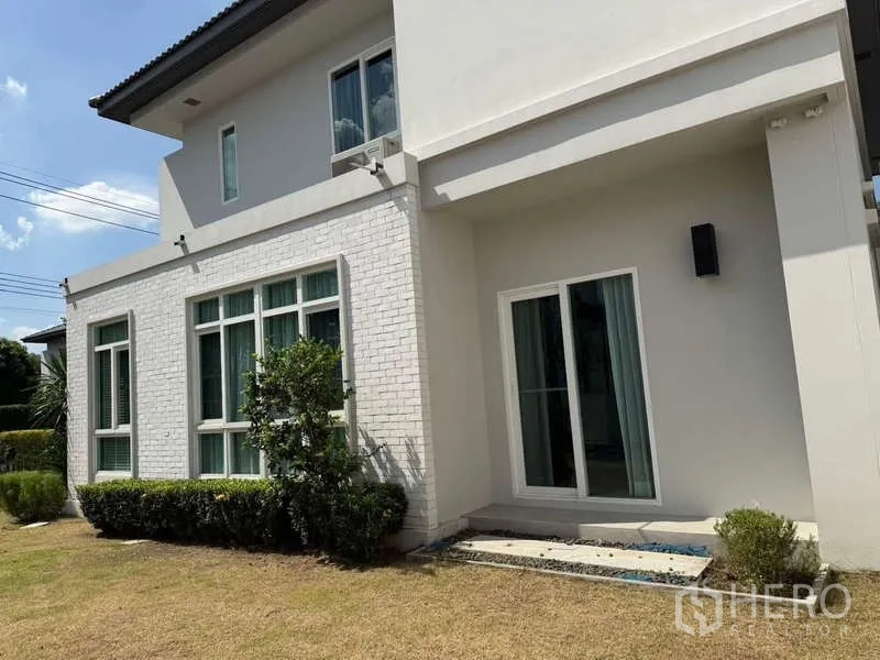 Detached House for rent or sale in Bang Bua Thong, Nonthaburi - Rear exterior featuring a sliding glass door, white brick accent wall, and landscaped lawn.