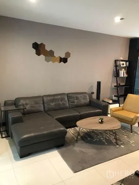 Townhouse for rent in Lat Phrao, Bangkok - Modern living room with a black leather sectional sofa, yellow accent chair and wall art.