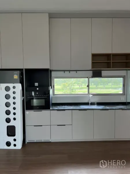 Detached House for rent in Saphan Sung, Bangkok - Sleek built-in kitchen with matte cabinets, black stone countertop and a window facing greenery.