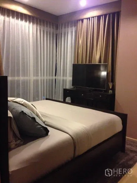 Condominium for rent in Watthana, Bangkok - Master bedroom with corner floor-to-ceiling windows, sheer drapes and a TV on a dresser.