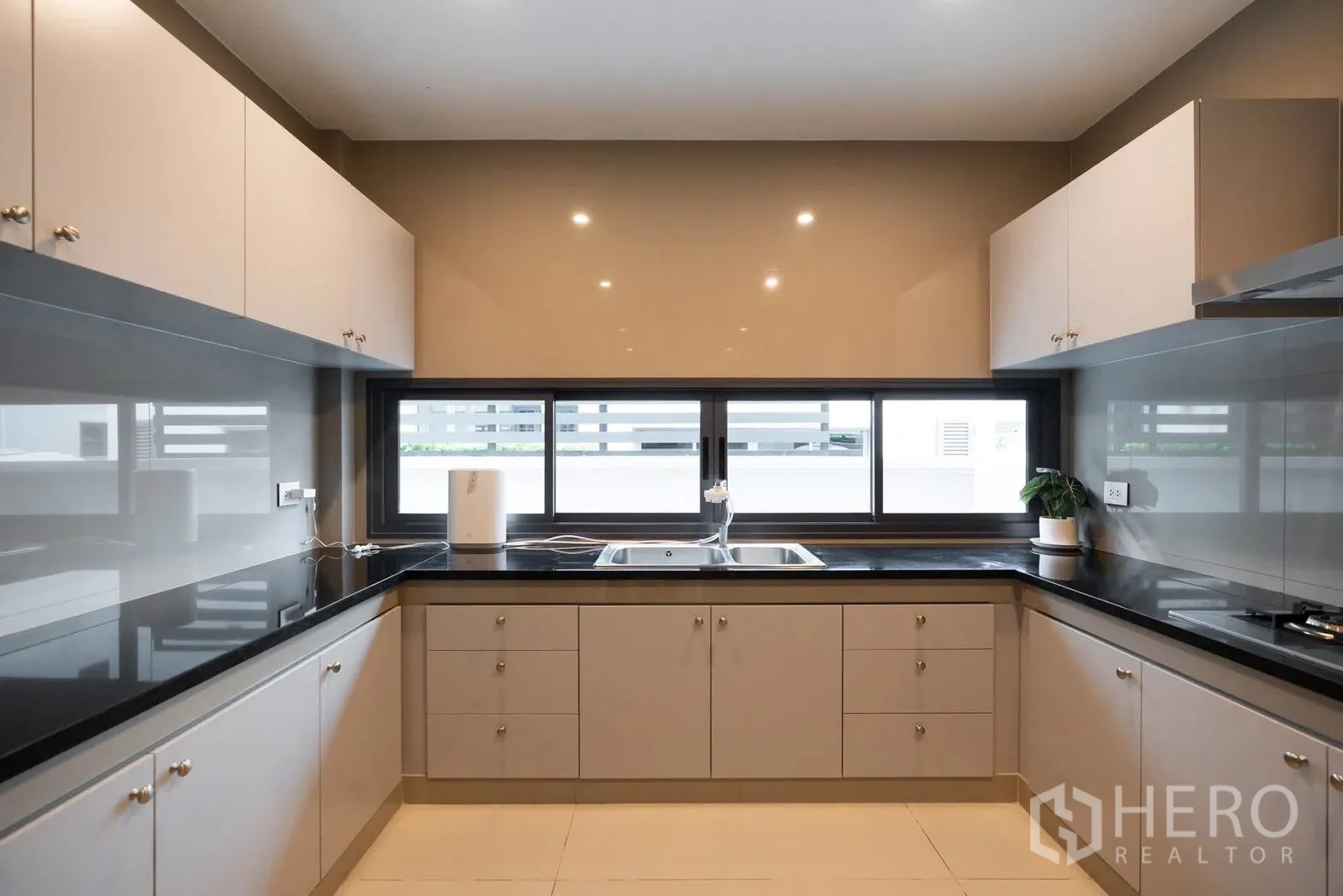 Detached House for rent or sale in Bang Kapi, Bangkok - Bright U-shaped kitchen with black stone countertops, twin sink, and sliding windows.