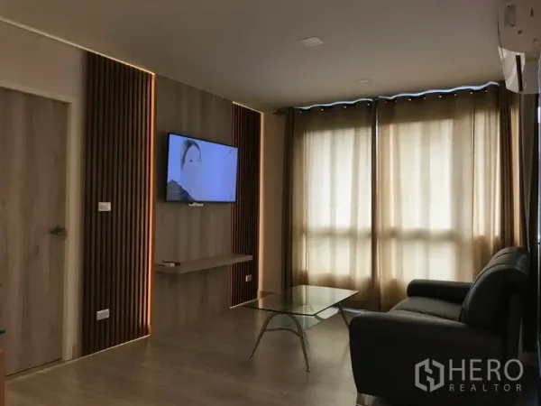 Condominium for rent in Watthana, Bangkok - Cozy lounge with leather sofa, mounted TV, and large windows with blackout curtains.