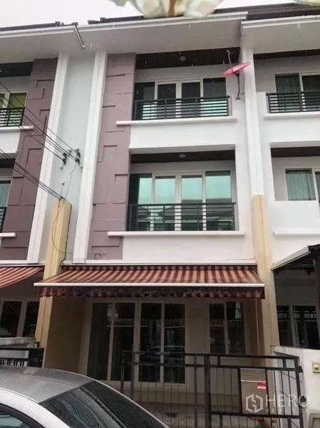 联排别墅 出租在Wang Thonglang, Bangkok - 曼谷旺通朗三层联排别墅外立面，带阳台、条纹遮阳篷与带门车位。