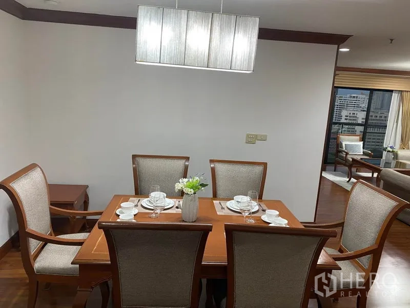 Condominium for rent in Watthana, Bangkok - Dining area set for six with wooden table, cushioned chairs and a modern pendant light.