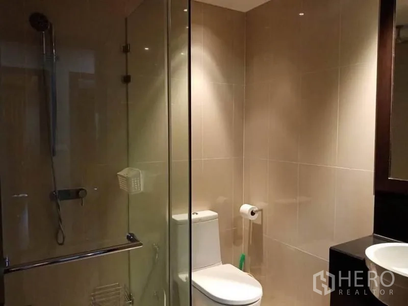 Condominium for rent in Sathon, Bangkok - Tiled bathroom featuring a glass-enclosed shower and toilet with warm lighting.