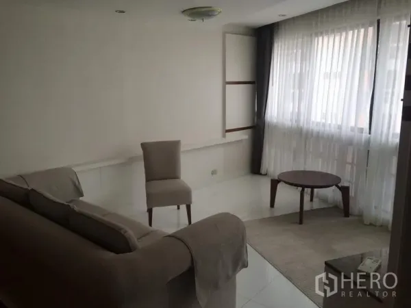 Condominium for rent in Khlong Toei, Bangkok - Bright secondary sitting room with sofa, accent chair and coffee table beside large sheer-draped windows at President Park.